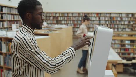 Hombre-Negro-Usando-Una-Pantalla-Digital-Interactiva-En-La-Biblioteca